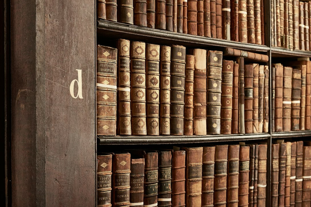 Shelf of old leather bound books in a dim library